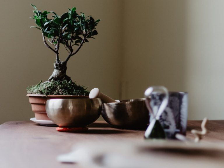 Sanduhr-Impulse? Bonsai-Baum in einem Topf, daneben Klangschalen und eine Sanduhr auf einem Tisch.