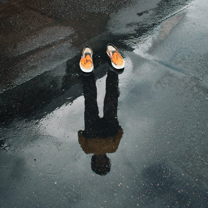 Reflexion einer Person mit farbigen Schuhen auf nassem Boden.