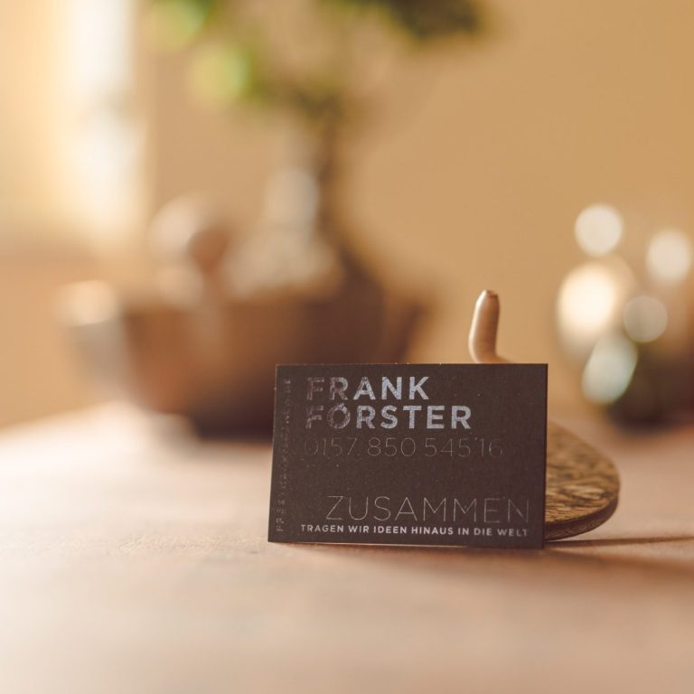 Visitenkarte von Frank Forster auf einem Holztisch mit unscharfem Hintergrund.