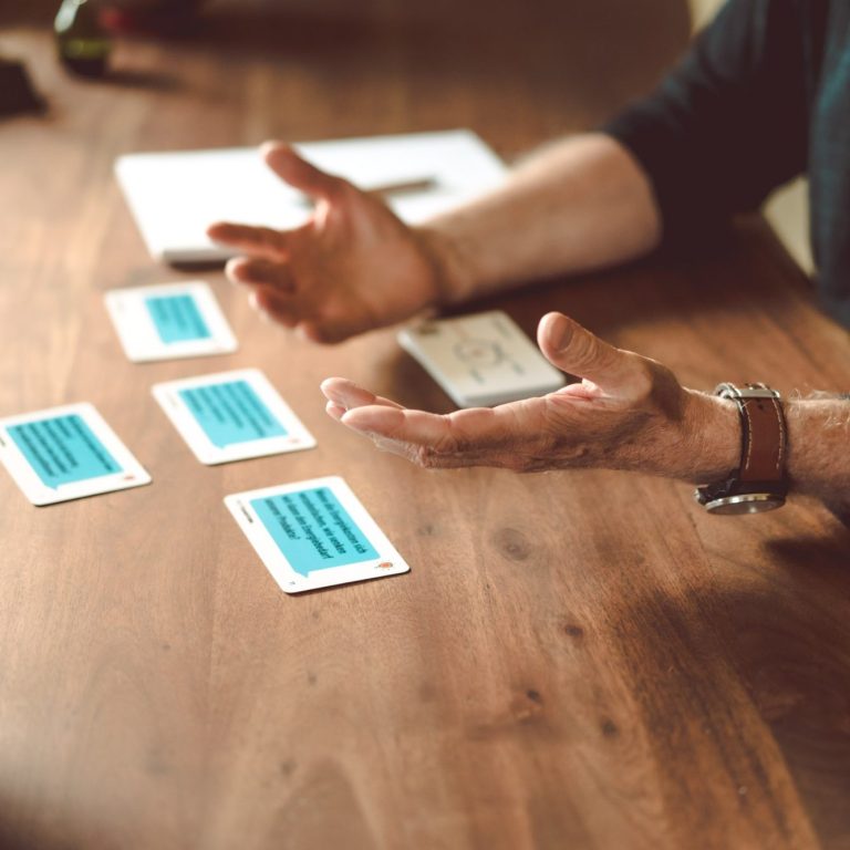 Zwei Hände deuten erklärend auf aufgedeckte Fragekarten eines Coaching-Tools.