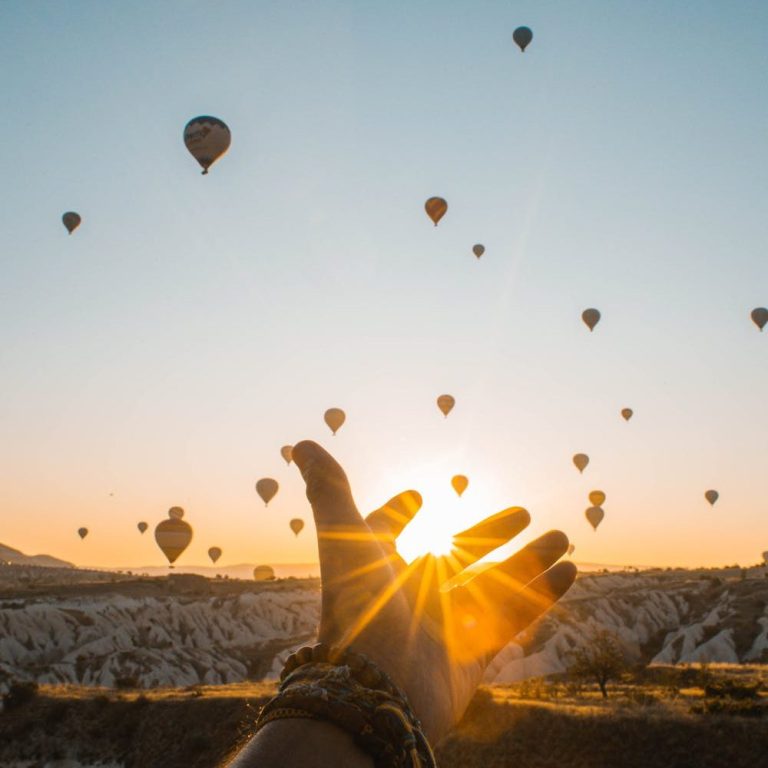 Händediagramm mit Sonnenaufgang und schwebenden Heißluftballons im Hintergrund.